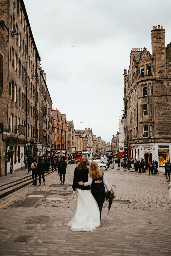 two brides in dress and suit walking in the wind