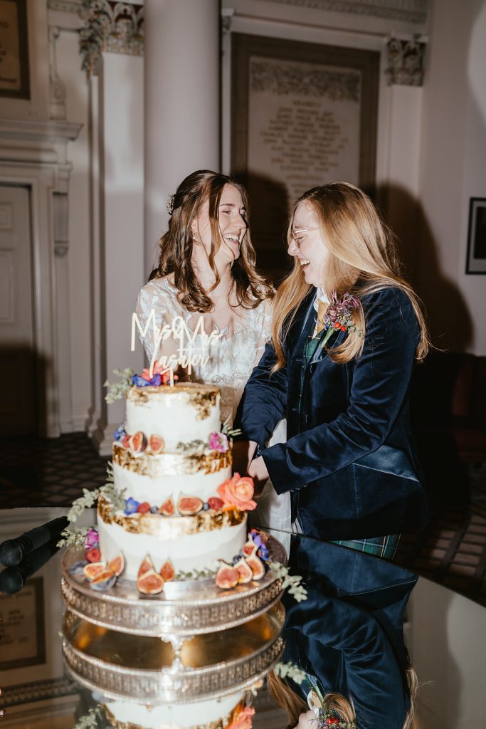 two brides in dress and suit cutting wedding cake