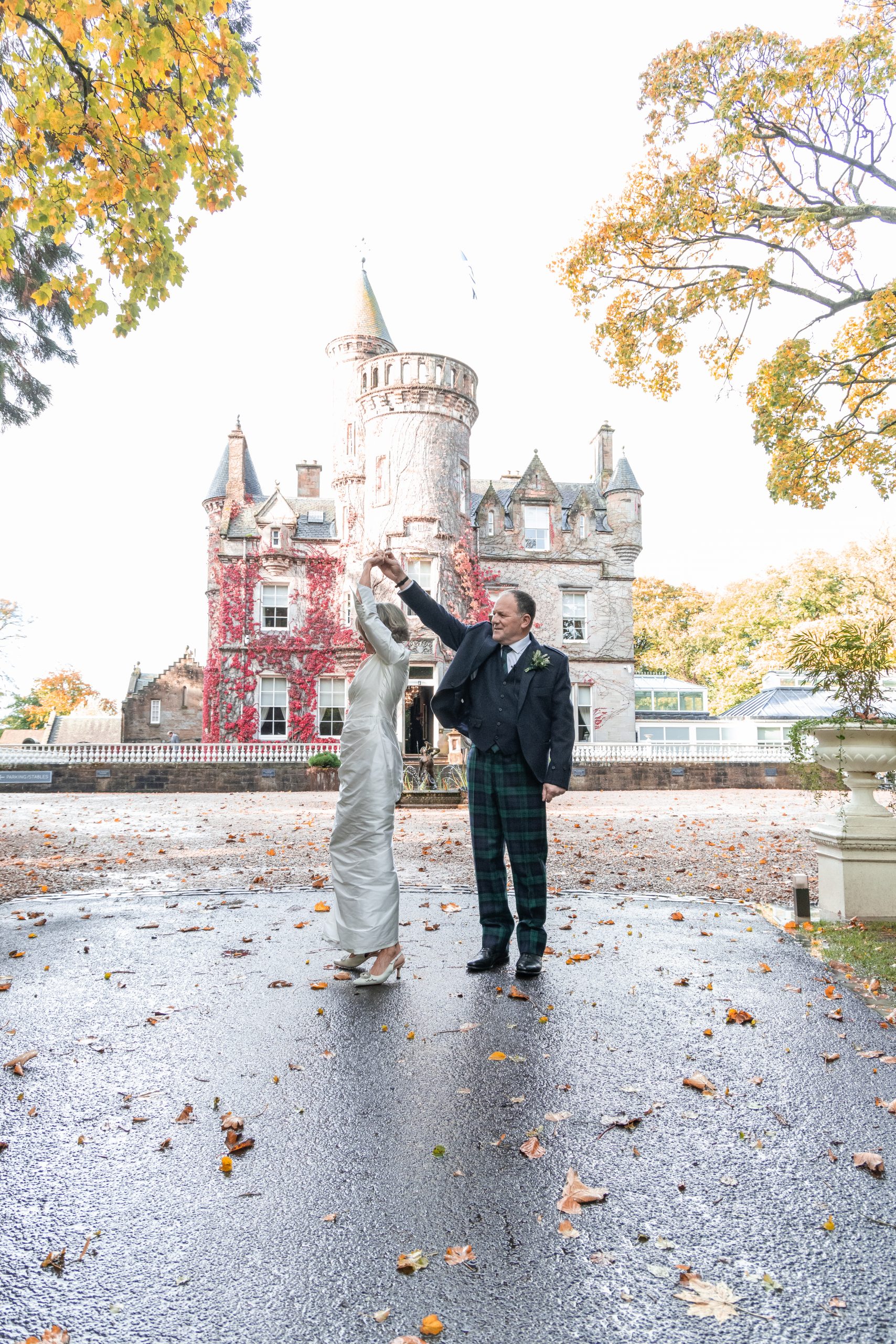 mature bride and groom dancing in front of Scottish Castle on their wedding day